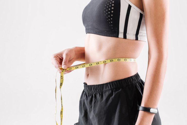 Close up portrait of a slim sportswoman measuring her waist with a yellow tape isolated over white background