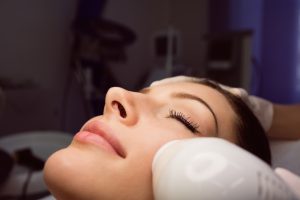 Dermatologist giving facial massage to patient through sonic lifting in clinic